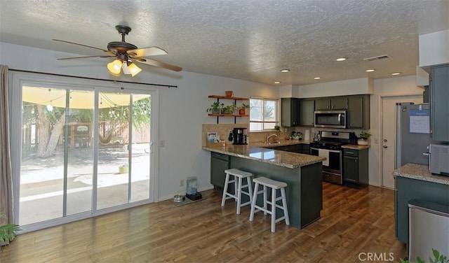 kitchen with stainless steel appliances, light stone countertops, a kitchen bar, dark hardwood / wood-style flooring, and kitchen peninsula