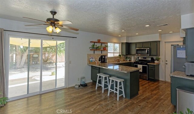 kitchen featuring a breakfast bar area, open shelves, appliances with stainless steel finishes, dark wood-type flooring, and a peninsula