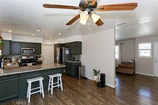 kitchen featuring appliances with stainless steel finishes, sink, kitchen peninsula, light stone countertops, and dark wood-type flooring