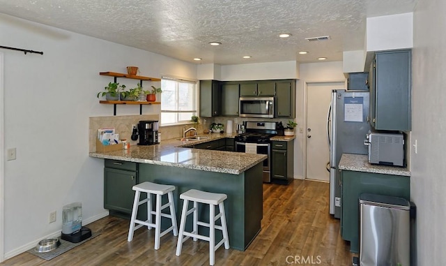 kitchen with appliances with stainless steel finishes, light stone counters, a kitchen bar, dark hardwood / wood-style flooring, and kitchen peninsula