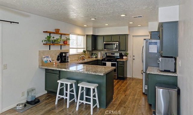 kitchen with visible vents, dark wood-style flooring, a peninsula, stainless steel appliances, and green cabinets