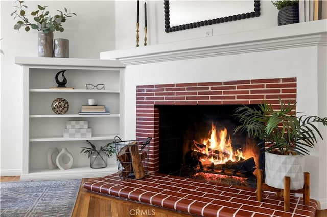 interior details with a brick fireplace, built in shelves, and hardwood / wood-style floors