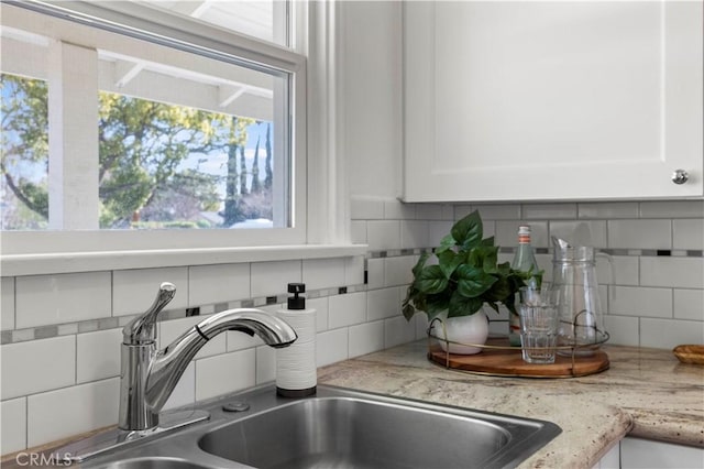 details with white cabinetry, sink, light stone counters, and decorative backsplash