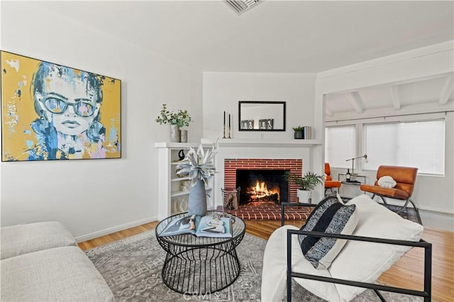 living room with a brick fireplace, wood-type flooring, and beamed ceiling