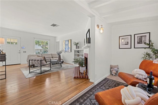 living room with a brick fireplace, beam ceiling, and light hardwood / wood-style flooring