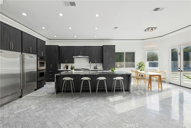 kitchen featuring appliances with stainless steel finishes, a center island with sink, a kitchen breakfast bar, and french doors