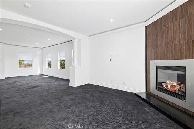 unfurnished living room featuring dark carpet, decorative columns, and a large fireplace