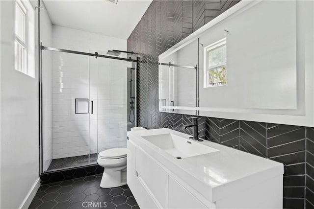 bathroom with toilet, a shower with shower door, tile walls, vanity, and tile patterned flooring