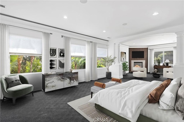 bedroom featuring a fireplace, dark colored carpet, and ornate columns