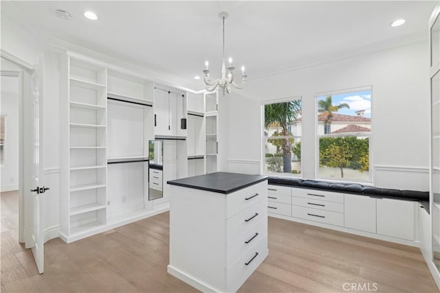 kitchen with white cabinetry, hanging light fixtures, an inviting chandelier, a center island, and light wood-type flooring