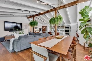 dining space with vaulted ceiling with beams, hardwood / wood-style floors, and track lighting