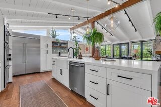 kitchen featuring white cabinetry, stainless steel appliances, lofted ceiling with beams, and hardwood / wood-style flooring