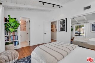 bedroom with beam ceiling, hardwood / wood-style flooring, and track lighting