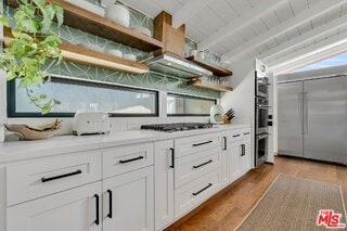 kitchen featuring white cabinetry, vaulted ceiling with beams, stainless steel appliances, and hardwood / wood-style flooring