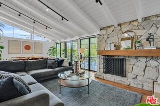 living room with wood-type flooring, a stone fireplace, rail lighting, and vaulted ceiling with beams