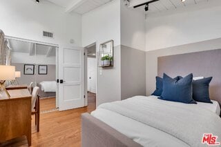 bedroom featuring hardwood / wood-style flooring, rail lighting, beamed ceiling, and a towering ceiling