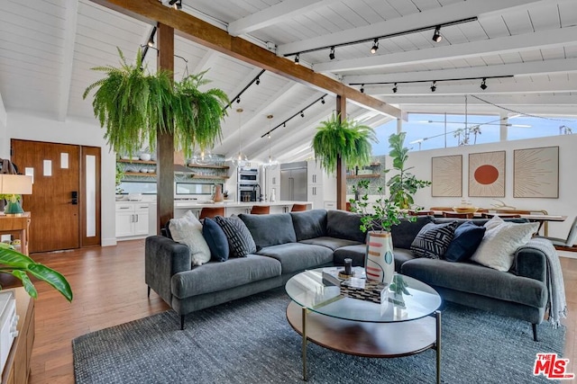 living room with rail lighting, vaulted ceiling with beams, hardwood / wood-style floors, and a chandelier