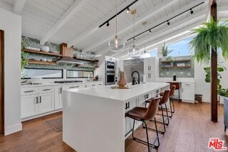 kitchen featuring white cabinetry, hanging light fixtures, a center island with sink, a kitchen breakfast bar, and hardwood / wood-style floors