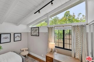 bedroom with hardwood / wood-style floors, track lighting, and lofted ceiling with beams