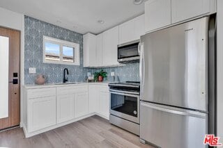 kitchen with white cabinetry, sink, backsplash, stainless steel appliances, and light hardwood / wood-style flooring