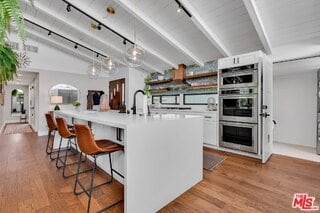 kitchen with pendant lighting, lofted ceiling with beams, white cabinets, a kitchen bar, and a center island with sink