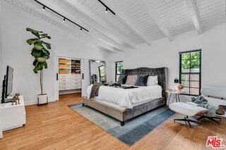 bedroom with beamed ceiling, wood-type flooring, rail lighting, and high vaulted ceiling