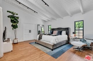 bedroom with track lighting, high vaulted ceiling, beam ceiling, and hardwood / wood-style floors