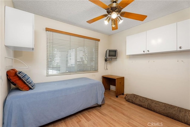 bedroom with ceiling fan, light hardwood / wood-style flooring, and a textured ceiling