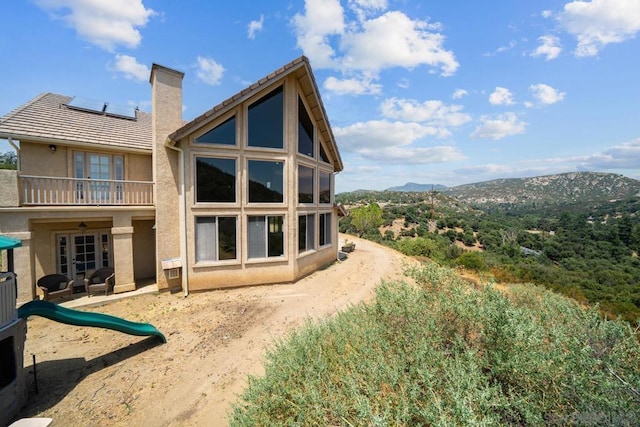 back of house featuring a playground, a balcony, a mountain view, and solar panels