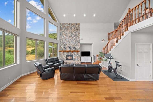 living room with plenty of natural light, a stone fireplace, high vaulted ceiling, and light wood-type flooring