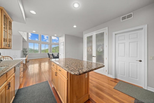 kitchen featuring light hardwood / wood-style flooring, a center island, light brown cabinetry, stainless steel dishwasher, and dark stone counters