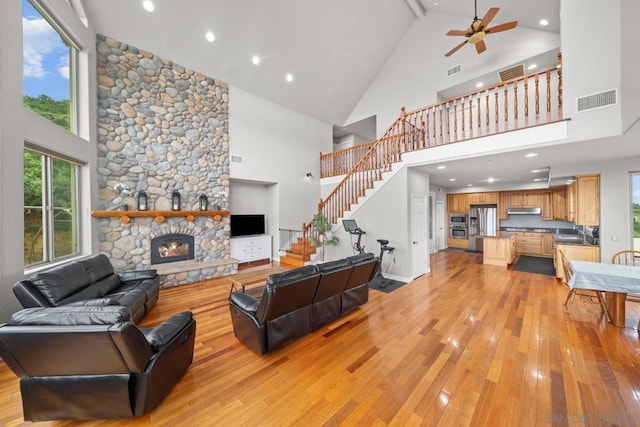 living room with ceiling fan, a stone fireplace, light wood-type flooring, and high vaulted ceiling