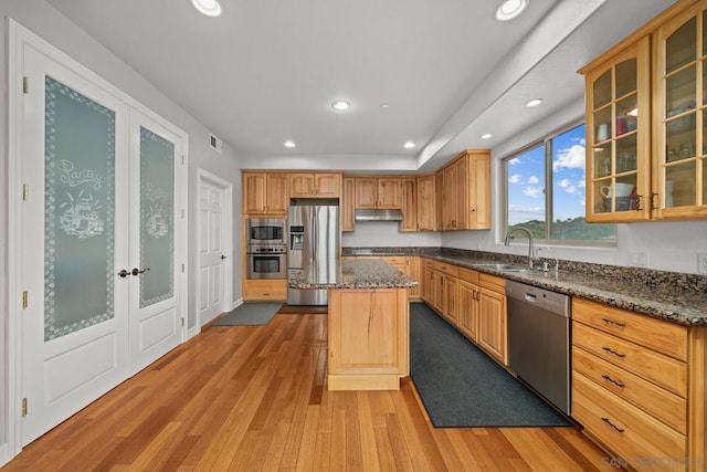 kitchen with sink, stainless steel appliances, a kitchen island, dark stone counters, and light wood-type flooring