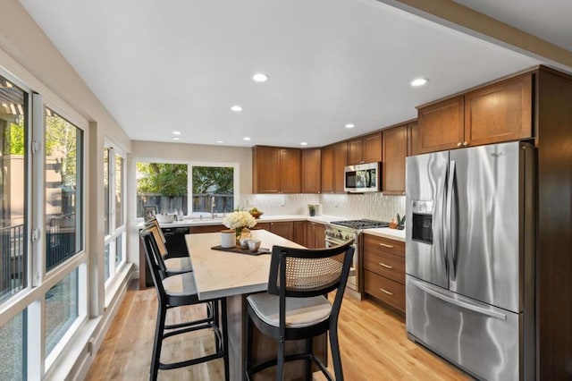 kitchen with a kitchen bar, light hardwood / wood-style flooring, stainless steel appliances, light stone countertops, and decorative backsplash