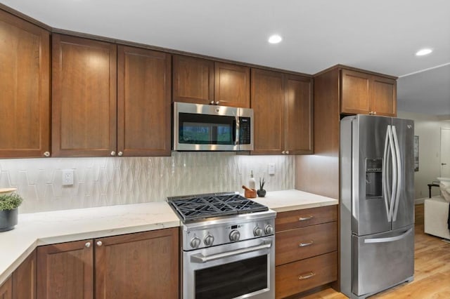 kitchen with tasteful backsplash, light stone counters, stainless steel appliances, and light hardwood / wood-style floors