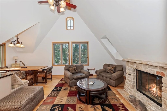 living room with ceiling fan, lofted ceiling, a stone fireplace, and light wood-type flooring