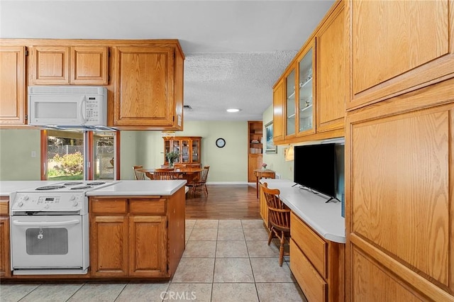 kitchen with light tile patterned flooring, built in desk, a textured ceiling, and white appliances