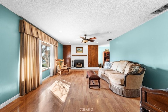 living room featuring ceiling fan, a brick fireplace, a textured ceiling, and light wood-type flooring