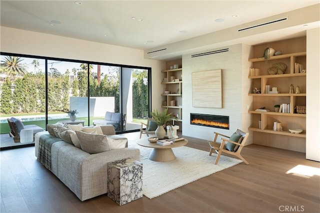 living room with wood-type flooring, a large fireplace, and built in shelves