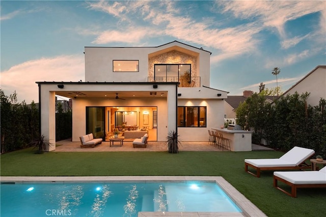 back house at dusk with an outdoor hangout area, a patio area, ceiling fan, and a bar