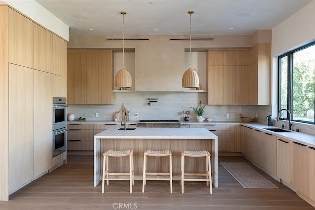 kitchen with a kitchen island with sink, sink, tasteful backsplash, and light brown cabinets