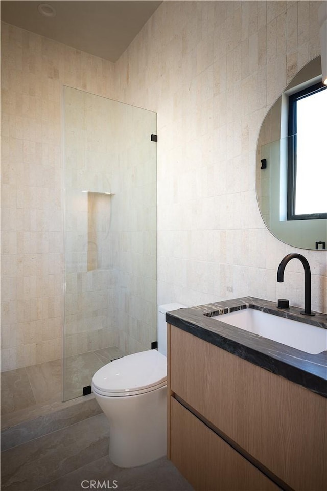 bathroom with walk in shower, vanity, toilet, and tile walls