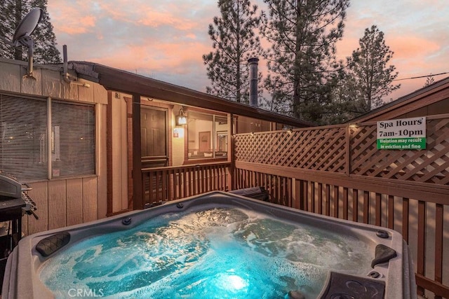 pool at dusk featuring a hot tub