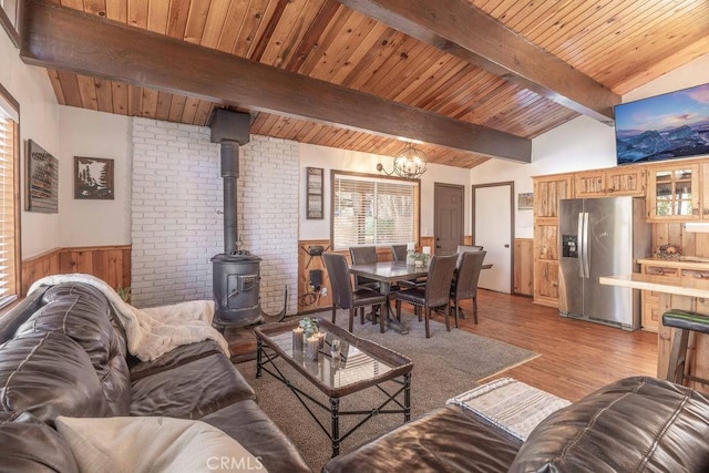 living room with a chandelier, lofted ceiling with beams, light wood-type flooring, wooden ceiling, and a wood stove