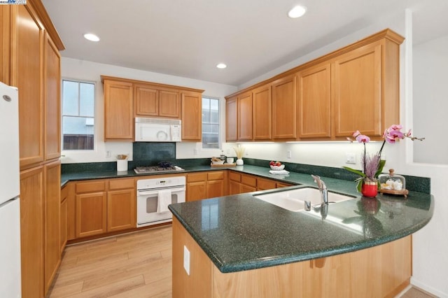 kitchen with sink, dark stone counters, light hardwood / wood-style floors, kitchen peninsula, and white appliances