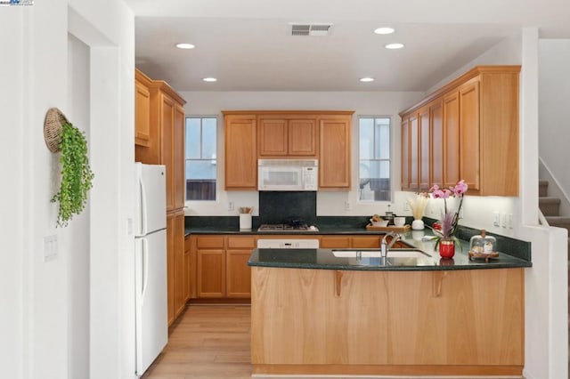 kitchen featuring sink, light wood-type flooring, kitchen peninsula, white appliances, and dark stone counters