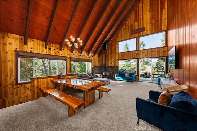 living room featuring wood ceiling, a wood stove, wooden walls, carpet floors, and beamed ceiling