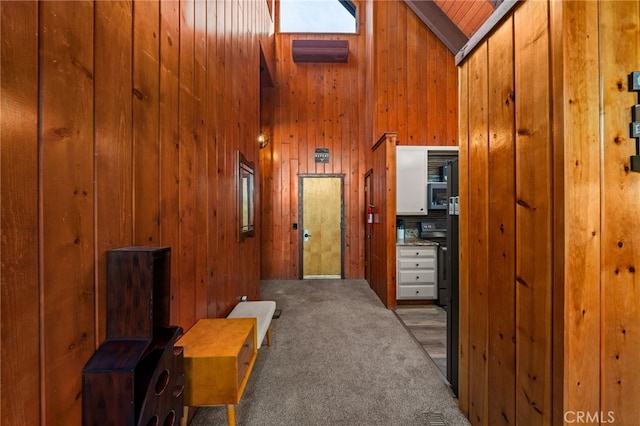 corridor featuring carpet flooring, wooden walls, and high vaulted ceiling