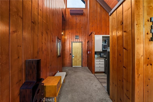 corridor featuring wooden walls, high vaulted ceiling, and carpet floors