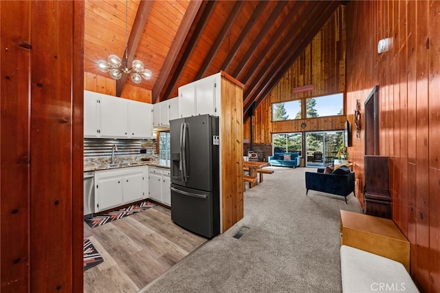 kitchen featuring an inviting chandelier, a sink, wood walls, stainless steel dishwasher, and black fridge